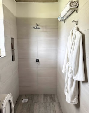 A modern shower stall with a handheld showerhead, a towel rack with a white towel, and a toilet in the corner. - Nagira Tranquility (Taveta)