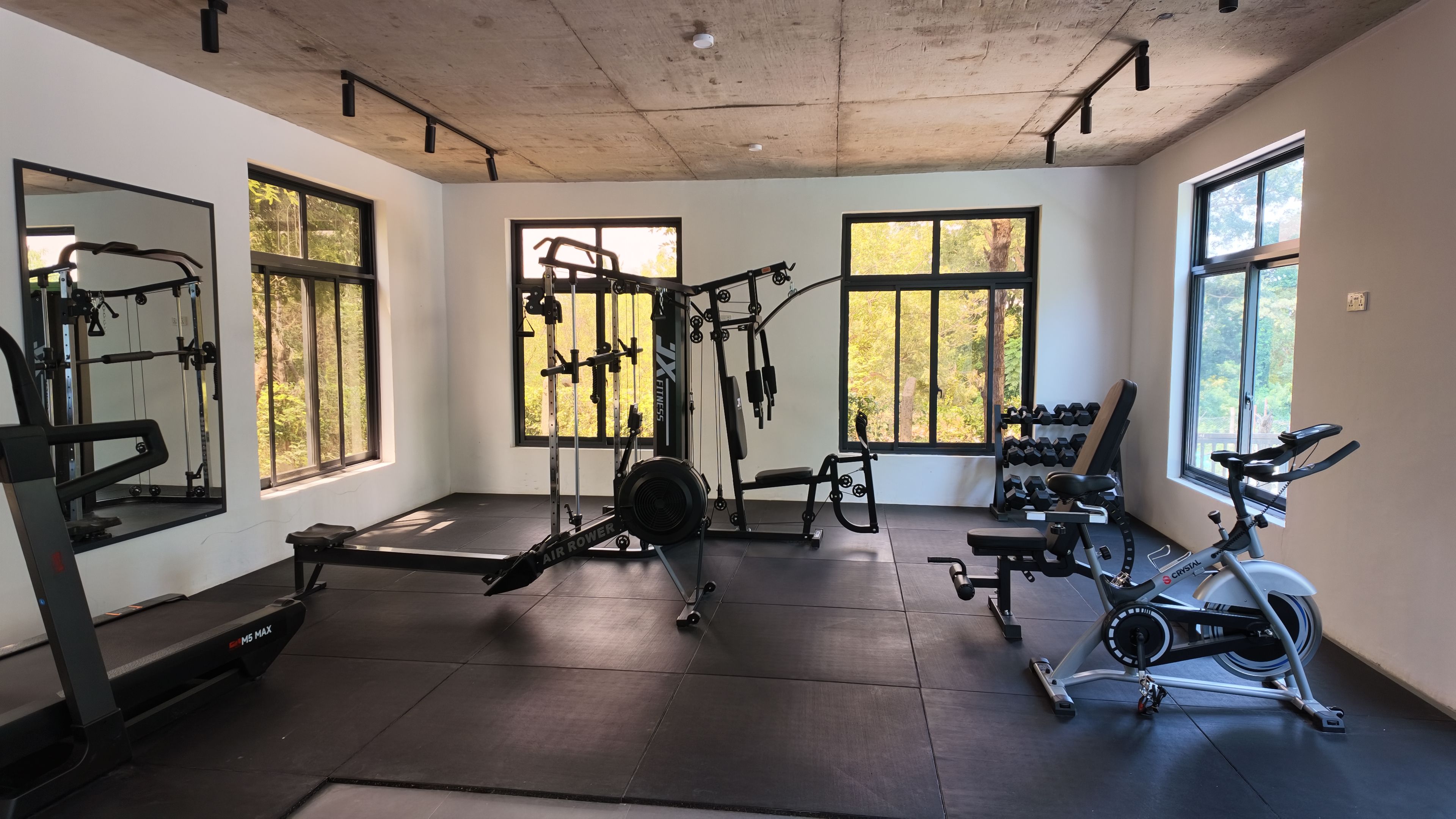 Un gimnasio con equipo de ejercicio, ventanas amplias y un techo con vigas a la vista.