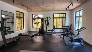 Un gimnasio con equipo de ejercicio, ventanas amplias y un techo con vigas a la vista.