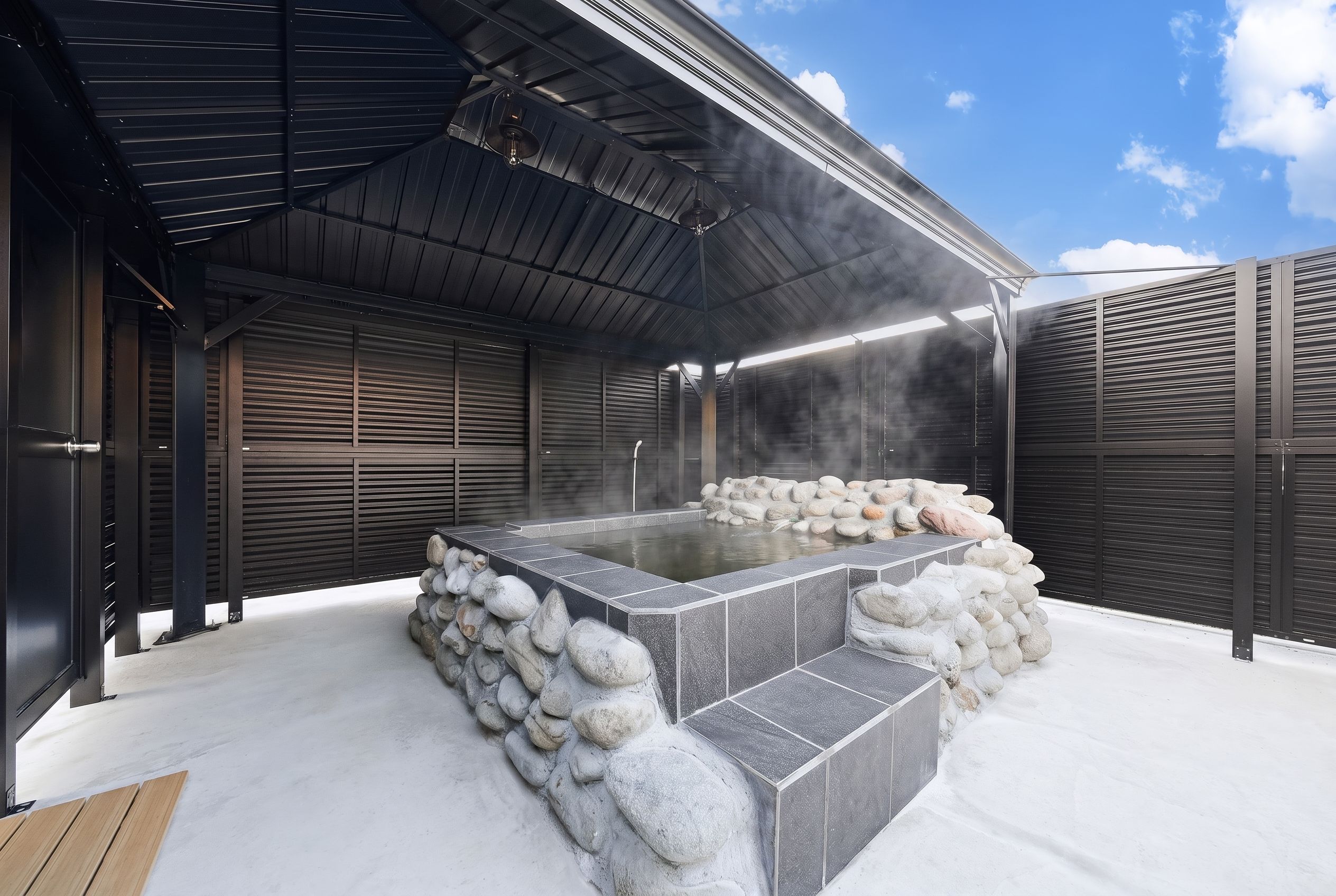 Eine Sauna mit einem Steingefäß, Dampf und einem überdachten Dach.