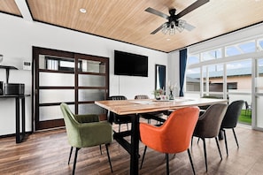 A modern dining area with a wooden table, colorful chairs, a ceiling fan, and a large window offering a view of the outdoors.