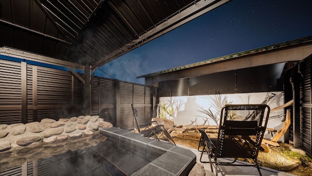 Een terras buiten met een hottub, barbecuehoek en uitzicht op de nachthemel.
