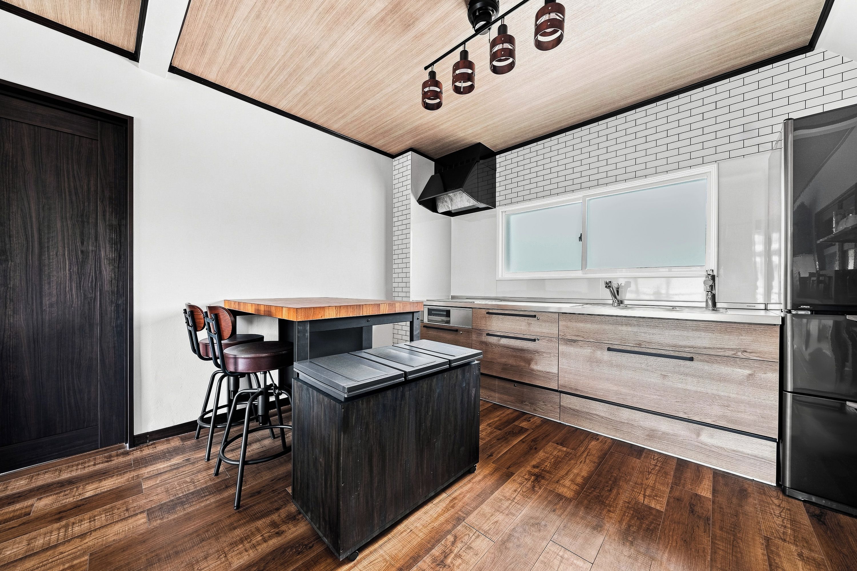 A modern kitchen with a wooden island, bar stools, a brick backsplash, and a large window.