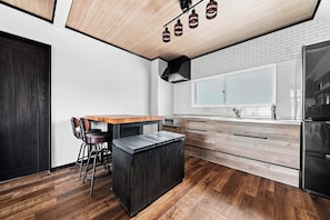 A modern kitchen with a wooden island, bar stools, a brick backsplash, and a large window.