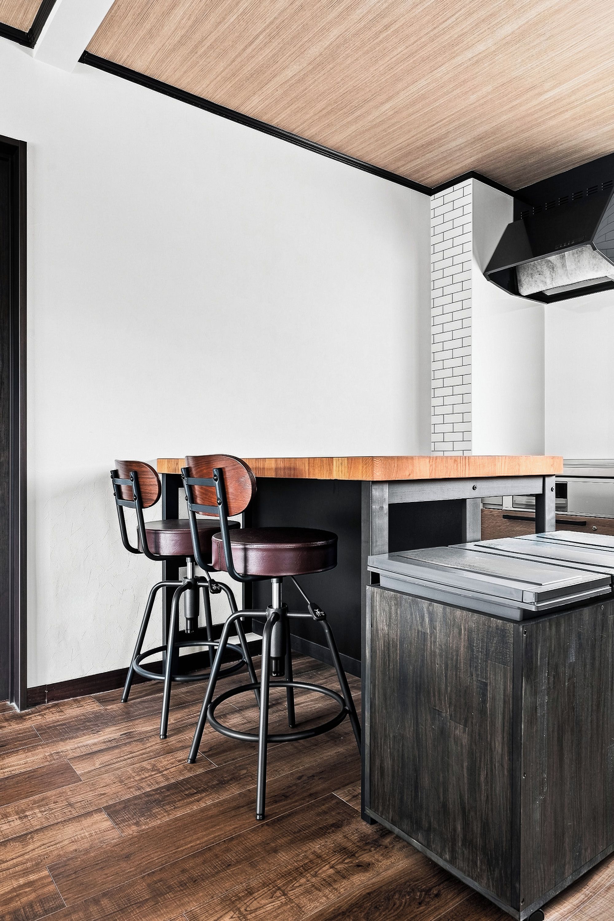 A modern kitchen with a wooden countertop, two bar stools, and a built-in brick oven.