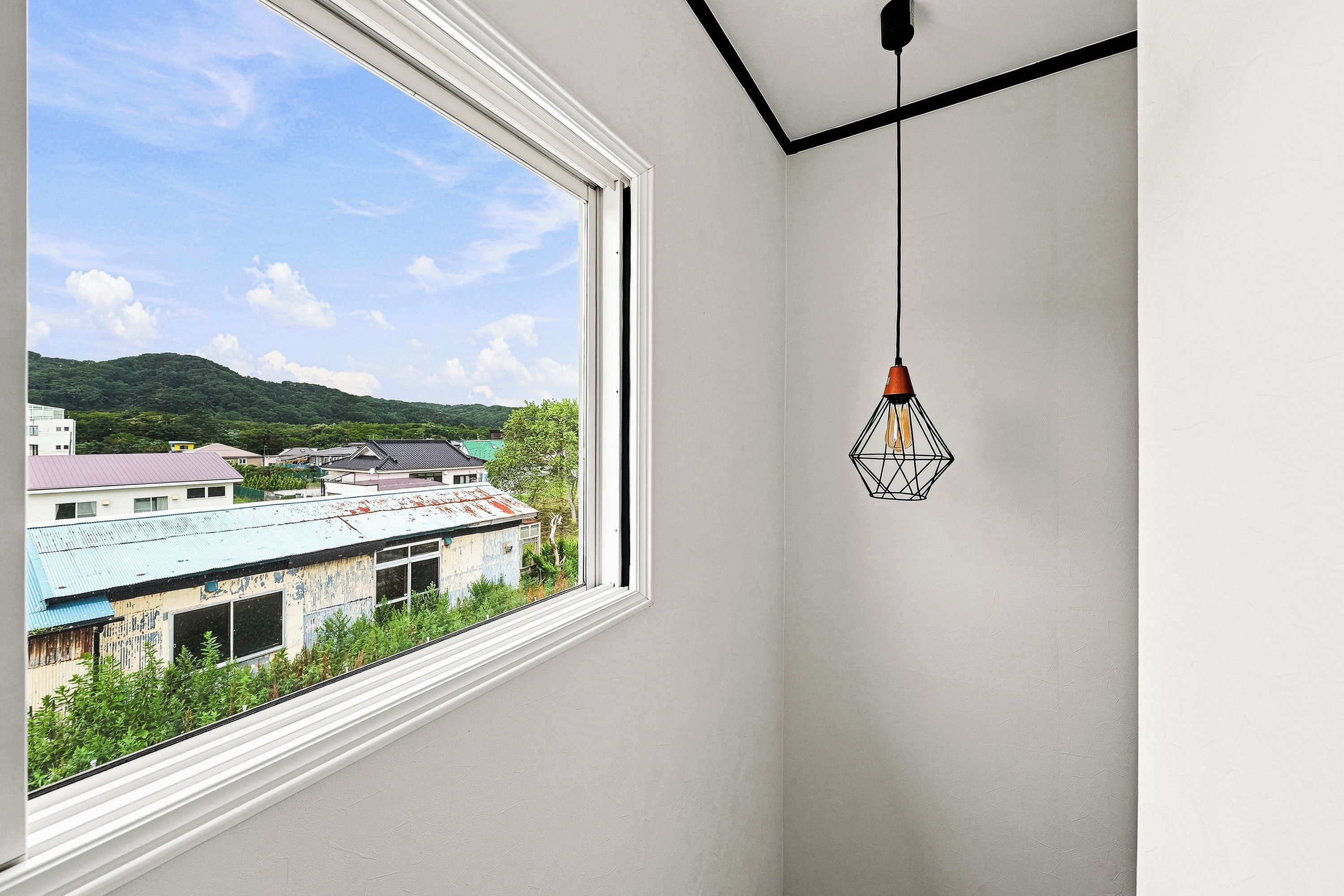 A room with a large window overlooking a building with a green roof and a view of a hill.