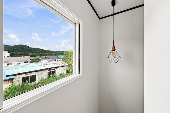 A room with a large window overlooking a building with a green roof and a view of a hill.