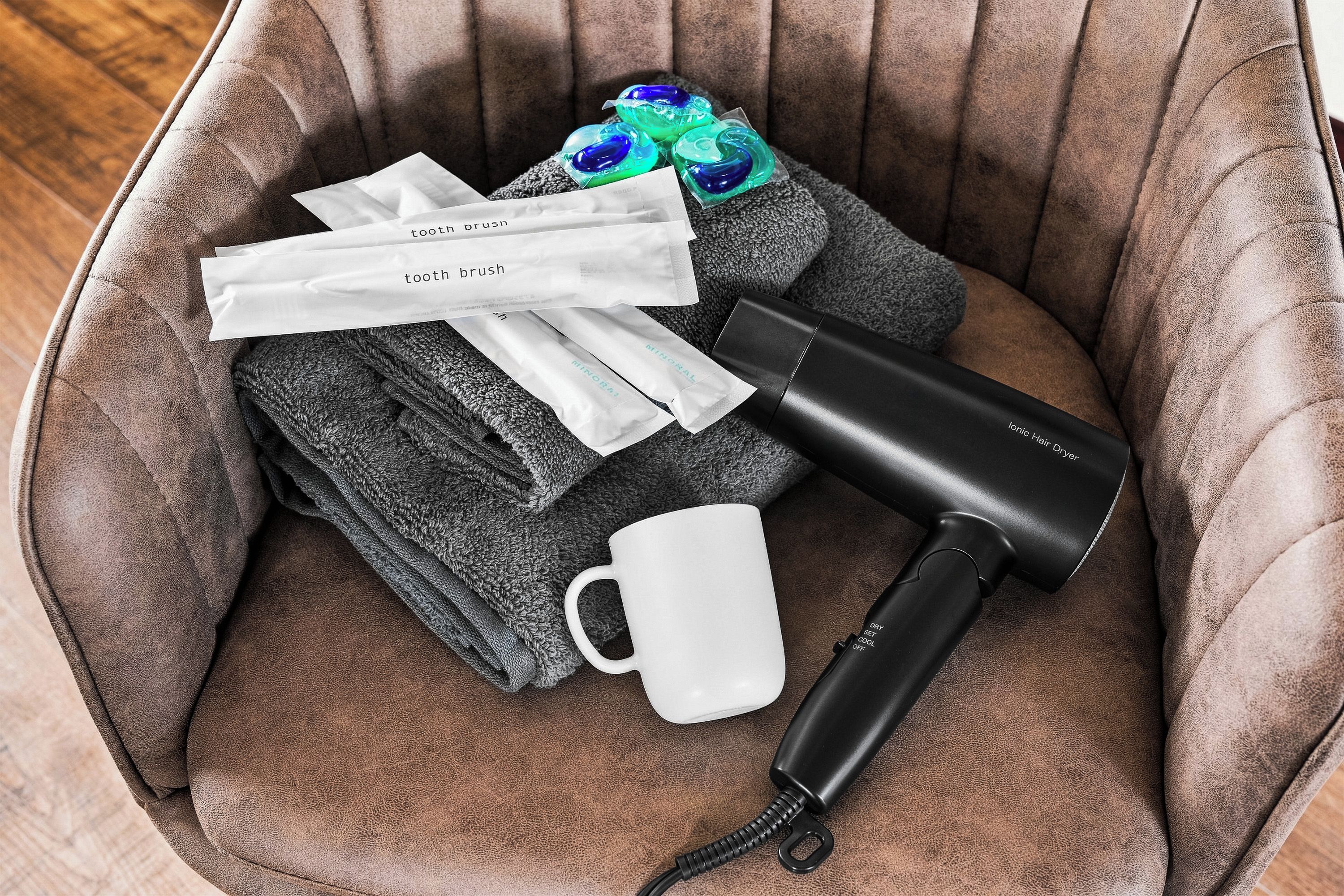 A brown upholstered chair with a white mug, a black hair dryer, and several gray towels.