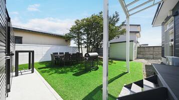A residential backyard with artificial grass, a barbecue grill, outdoor furniture, and a clear sky.