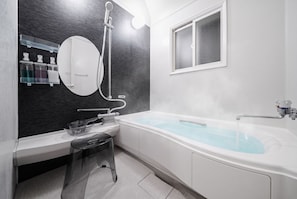 Une salle de bain moderne équipée d’une baignoire, d’une douche, d’un meuble-lavabo avec un miroir et d’une fenêtre.
