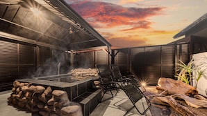 Een terras buiten met een stenen openhaard, zitplaatsen en uitzicht op de ondergaande zon.