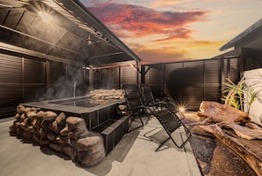 Une terrasse extérieure avec une cheminée en pierre, des sièges et une vue sur le coucher du soleil.
