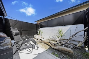 A modern outdoor seating area with a metal chair and a table, surrounded by rocks and a large log.