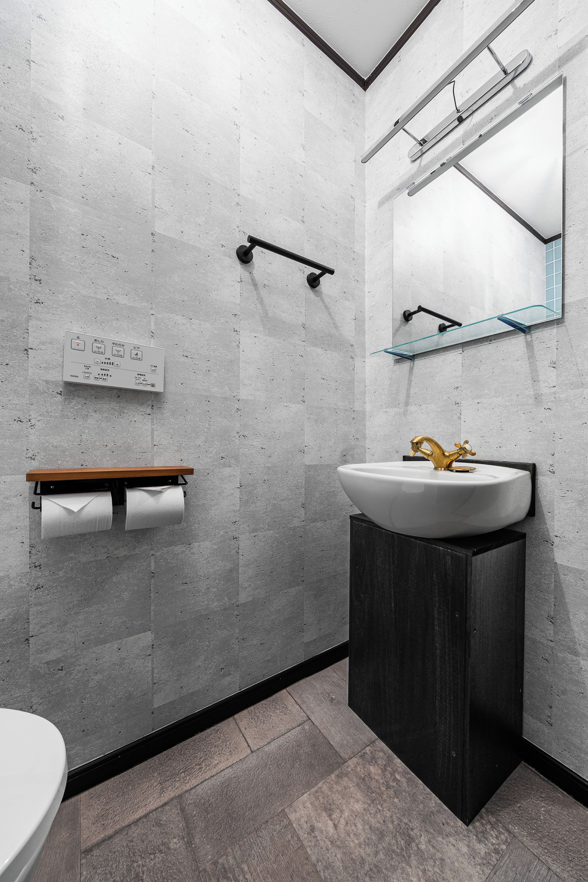 A modern bathroom with a toilet, a sink with a gold faucet, a mirror, and a towel dispenser.