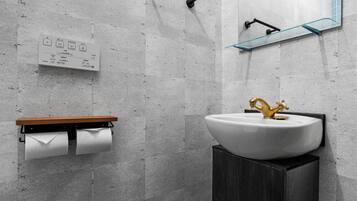 A modern bathroom with a toilet, a sink with a gold faucet, a mirror, and a towel dispenser.