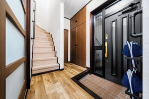 Un pasillo con una escalera de madera, una puerta negra con un panel de vidrio y un zapatero con zapatos.