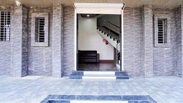 A building entrance with a staircase leading to an upper level, flanked by stone walls and a metal railing.