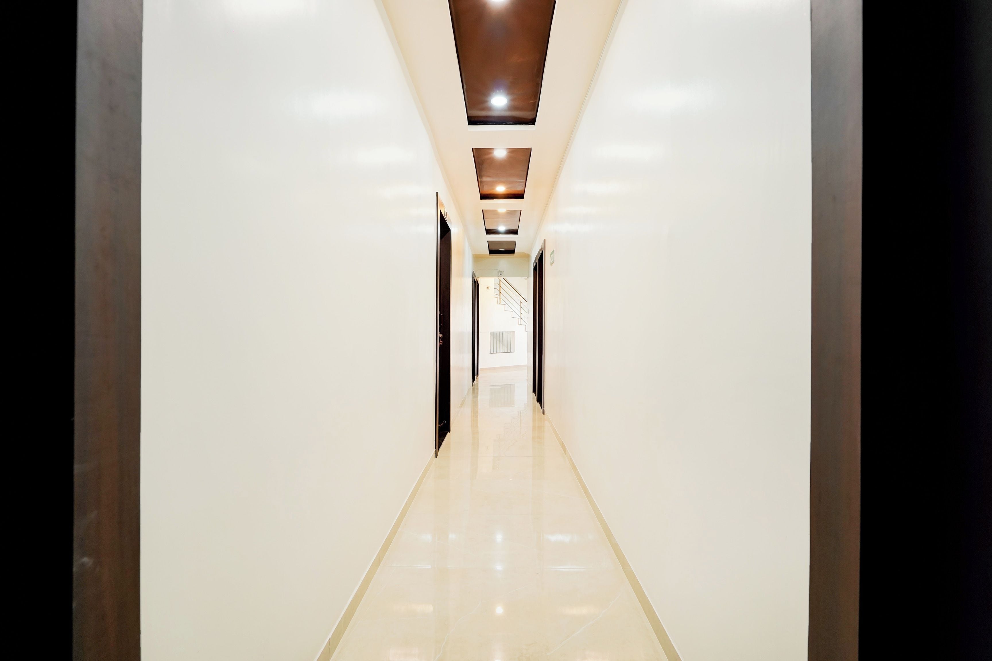 Un pasillo moderno y bien iluminado, con piso brillante, que conduce a una escalera y una puerta al final.