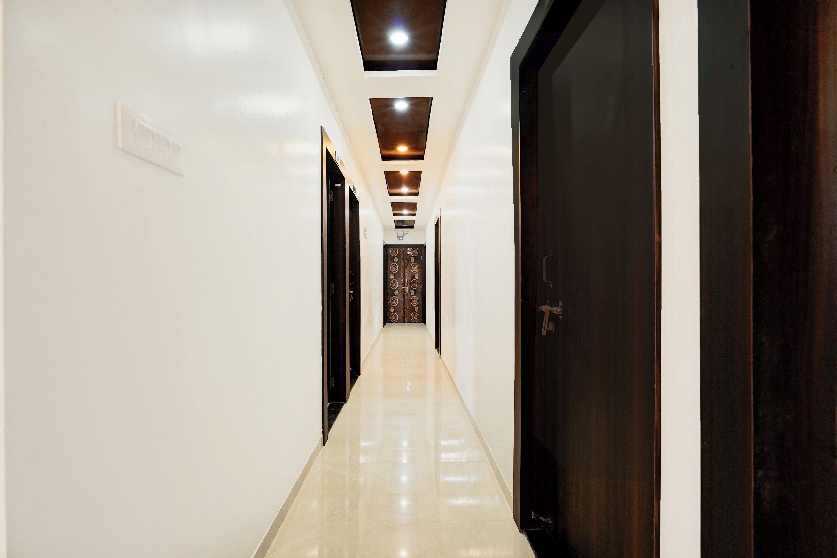 A hallway with a glossy floor, dark wooden doors, and recessed lighting.