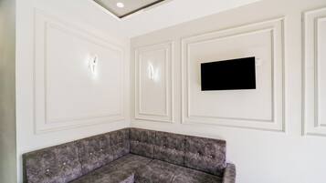 Quarto com sofá seccional, teto rebaixado e televisão de tela plana fixada na parede.