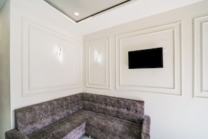Una habitación con sofá modular, techo empotrado y televisor de pantalla plana montado en la pared.