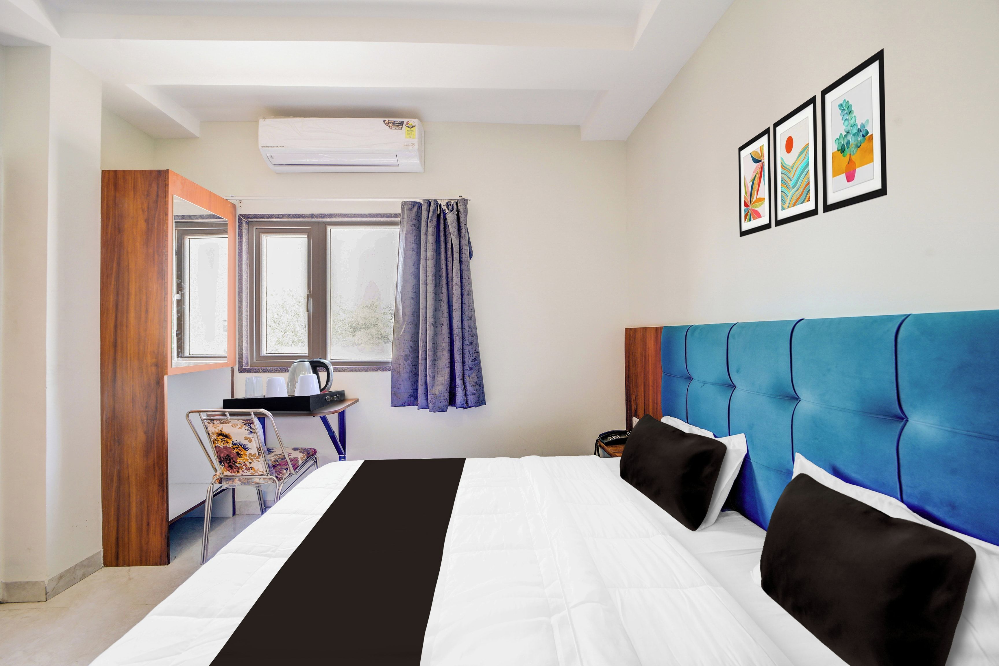 Quarto de hotel com cama, escrivaninha, cadeira, ar condicionado e janela com cortinas.
