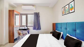 Quarto de hotel com cama, escrivaninha, cadeira, ar condicionado e janela com cortinas.