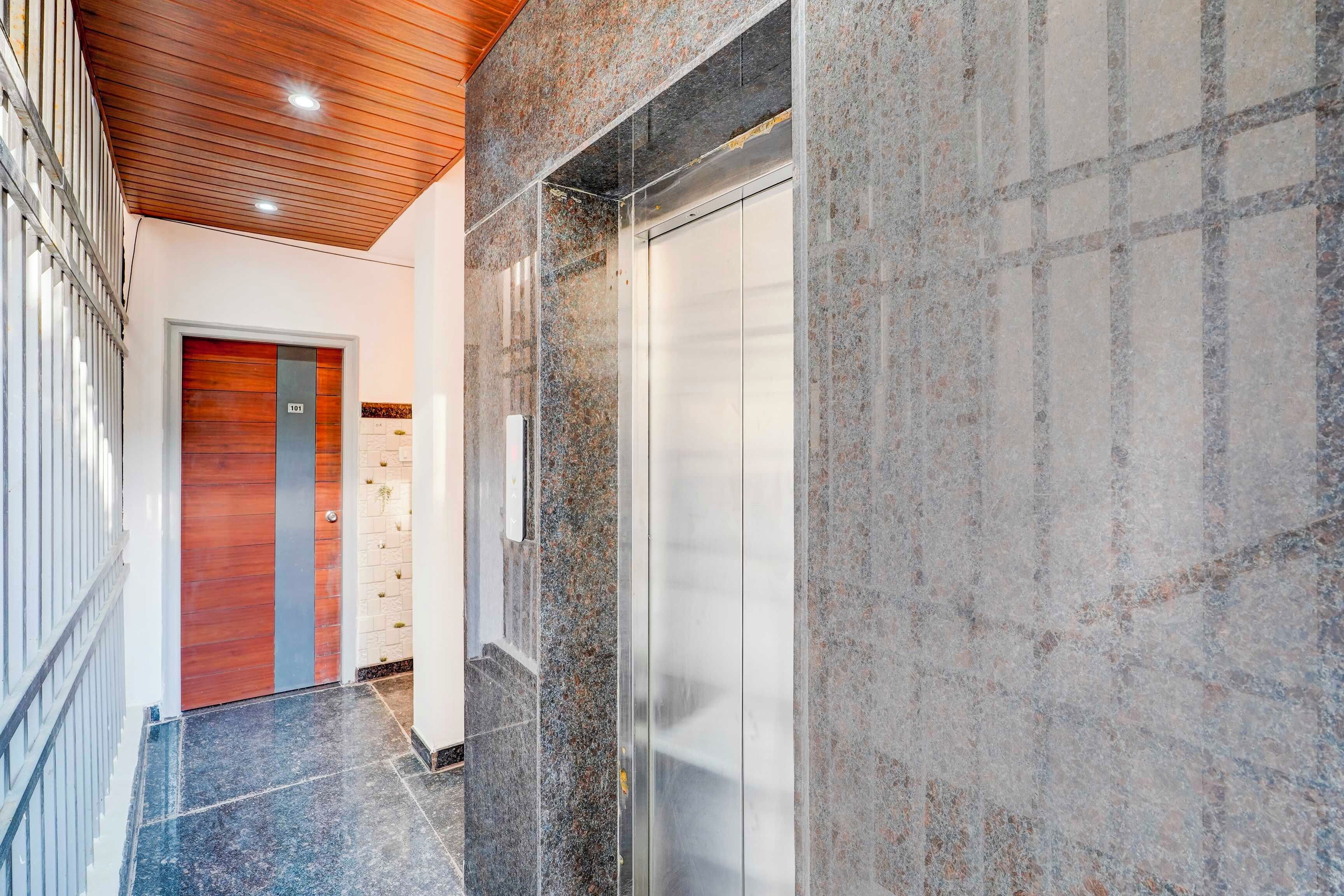 A modern elevator with a metallic finish, a wooden door with a number plate, and a corridor with a tiled floor.