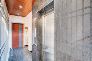 A modern elevator with a metallic finish, a wooden door with a number plate, and a corridor with a tiled floor.