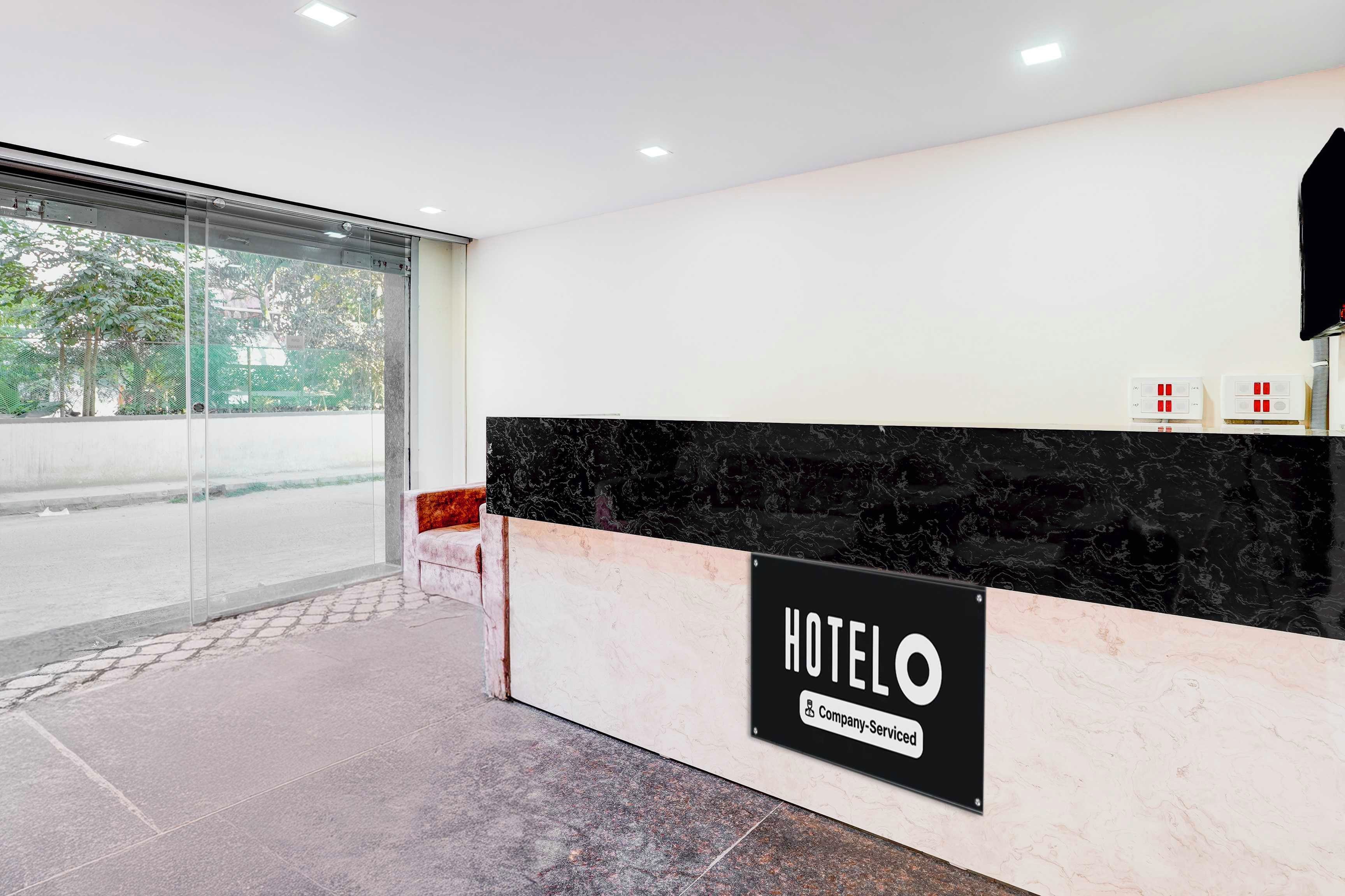 Un'area reception di un hotel con un bancone in marmo, un ingresso con porta in vetro e una segnaletica che indica servizio alberghiero aziendale.