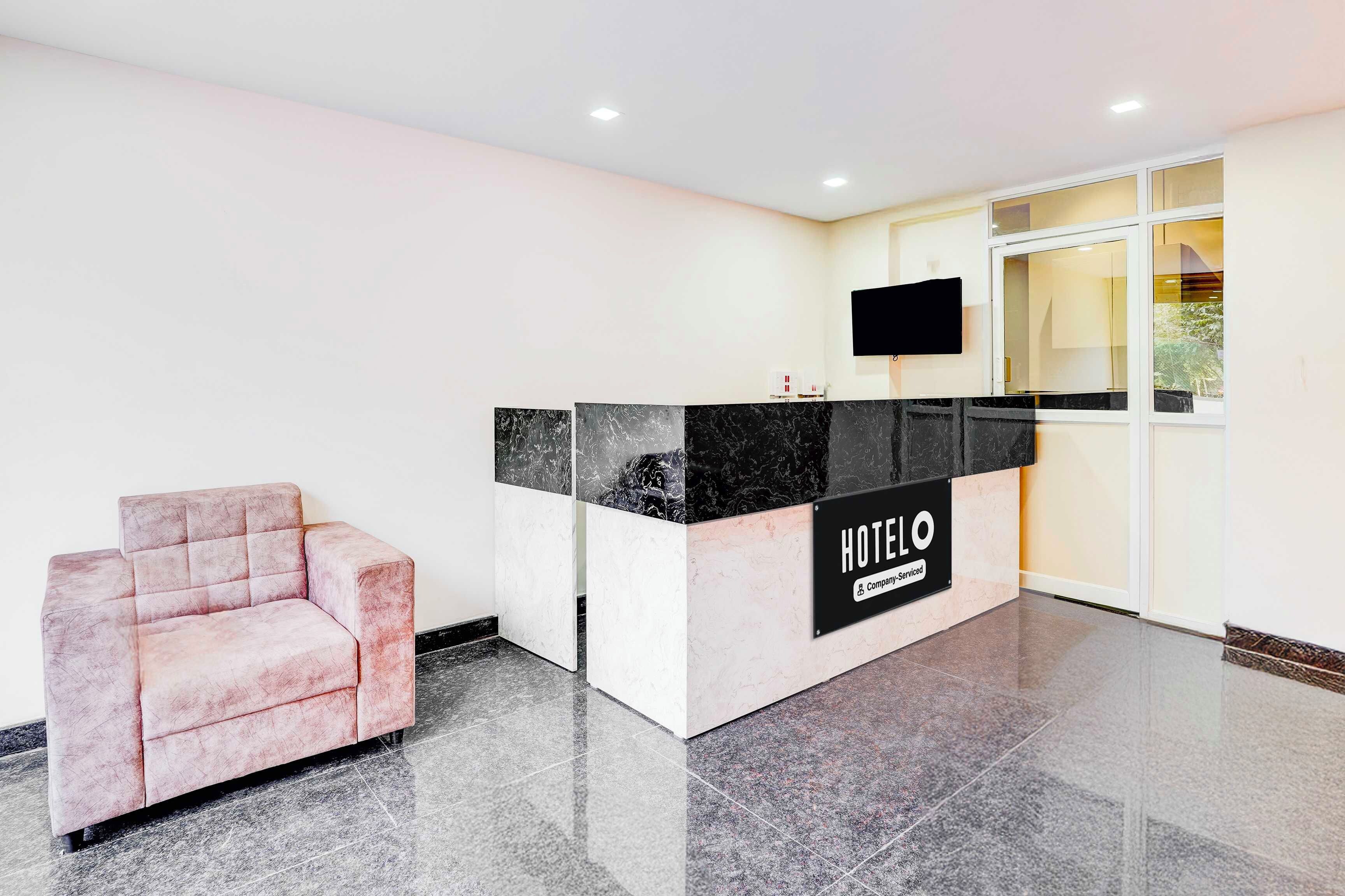 A hotel reception area with a marble counter, a flat-screen TV, and a pink armchair.