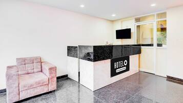 A hotel reception area with a marble counter, a flat-screen TV, and a pink armchair.