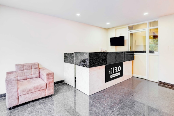 A hotel reception area with a marble counter, a flat-screen TV, and a pink armchair. - Townhouse Bhattrahalli Lakeview (Bengaluru)