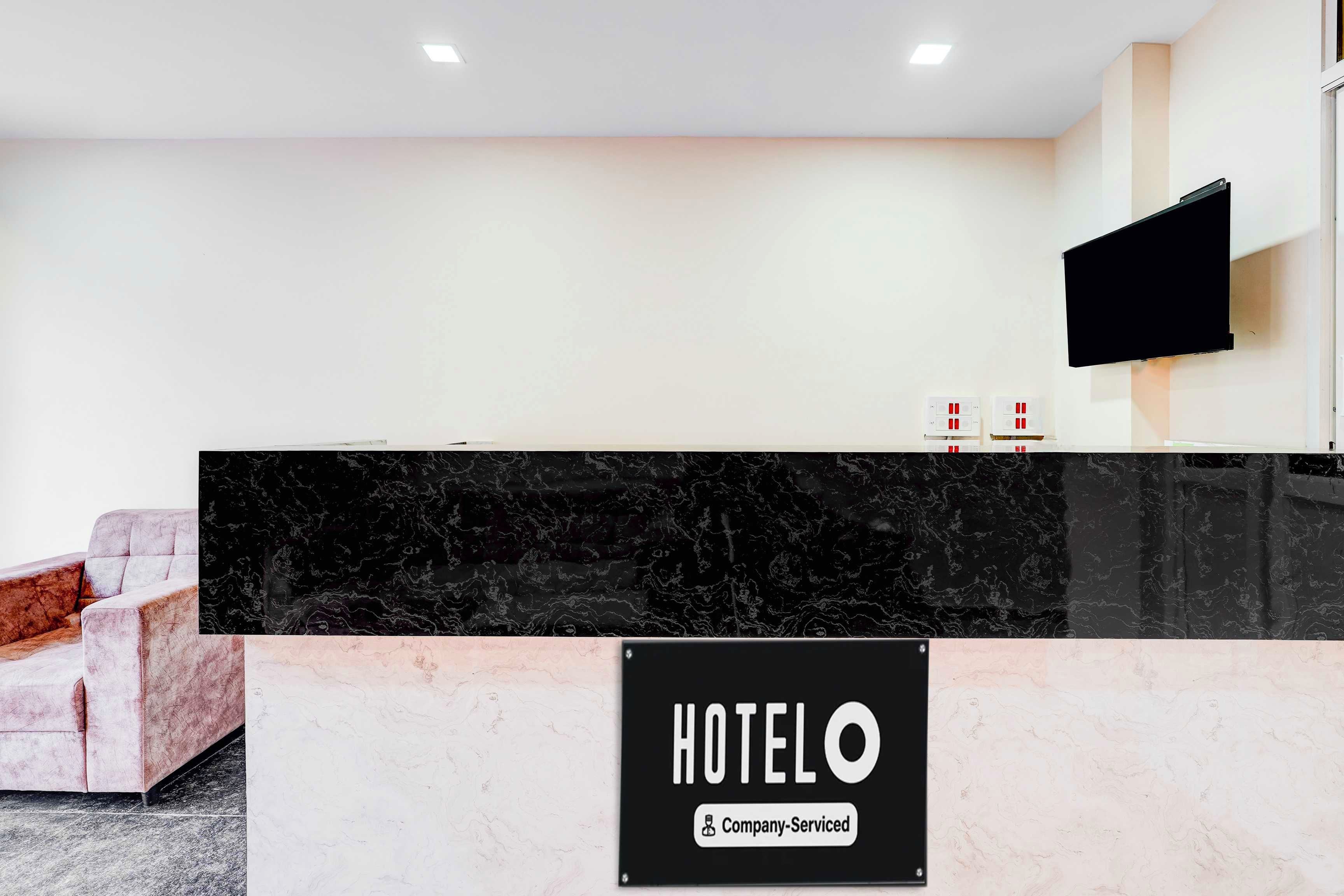 A hotel reception desk with a marble countertop, a flat-screen TV mounted on the wall, and a sign indicating the hotel is company-serviced.