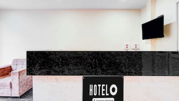 A hotel reception desk with a marble countertop, a flat-screen TV mounted on the wall, and a sign indicating the hotel is company-serviced.