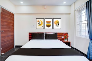 Hotellihuone, jossa on sänky, yöpöytä, seinään asennettu ilmastointilaite ja ikkuna, jossa on verhot.