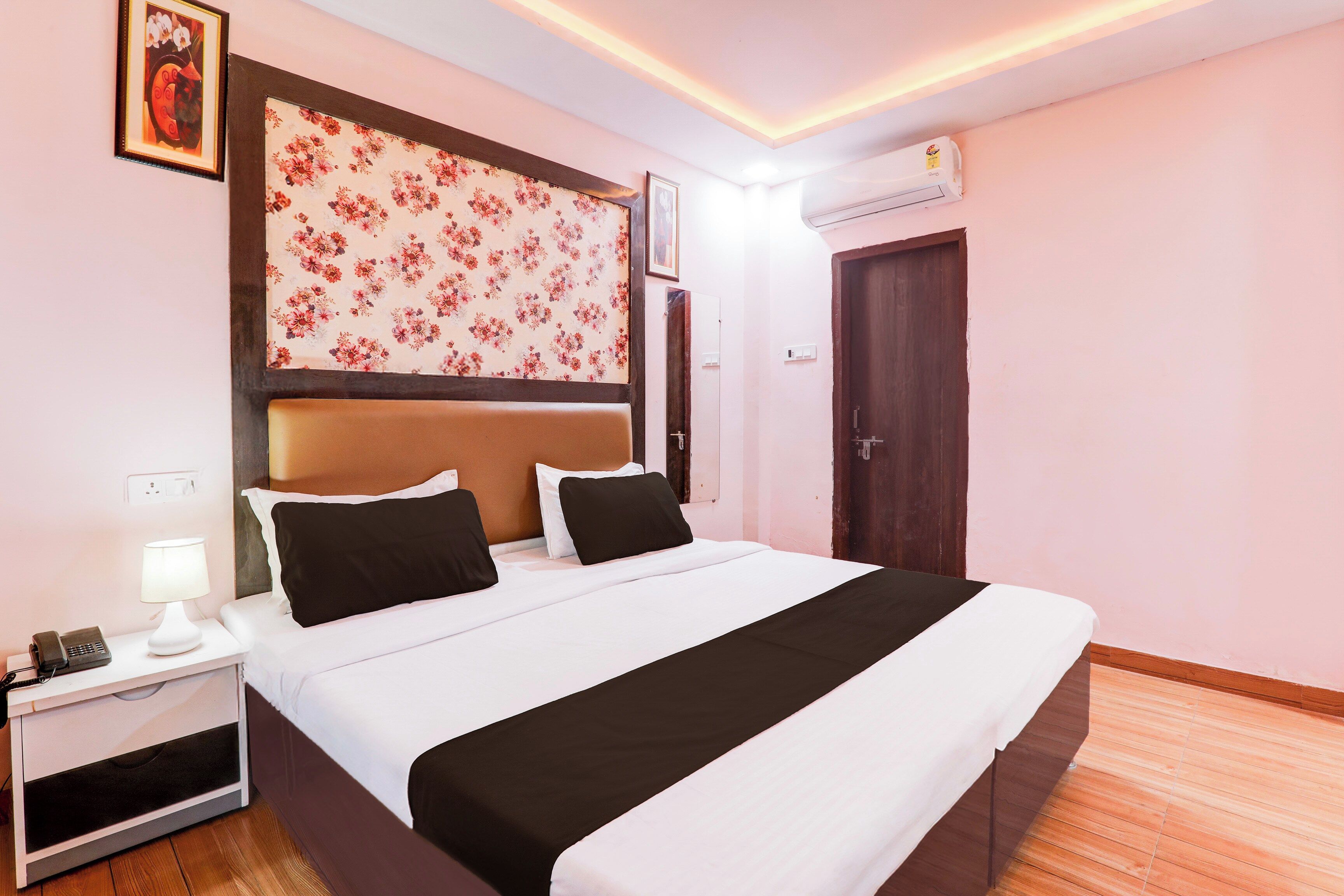 A hotel room with a bed, bedside table, lamp, and an air conditioning unit.