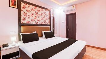 A hotel room with a bed, bedside table, lamp, and an air conditioning unit.