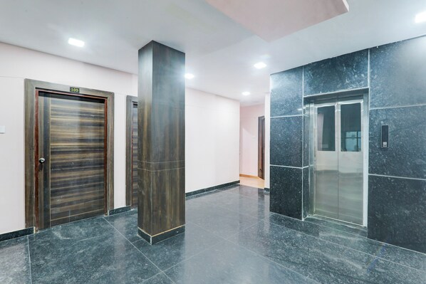 A modern hallway with a closed elevator, a door with a number plate, and a tall pillar.