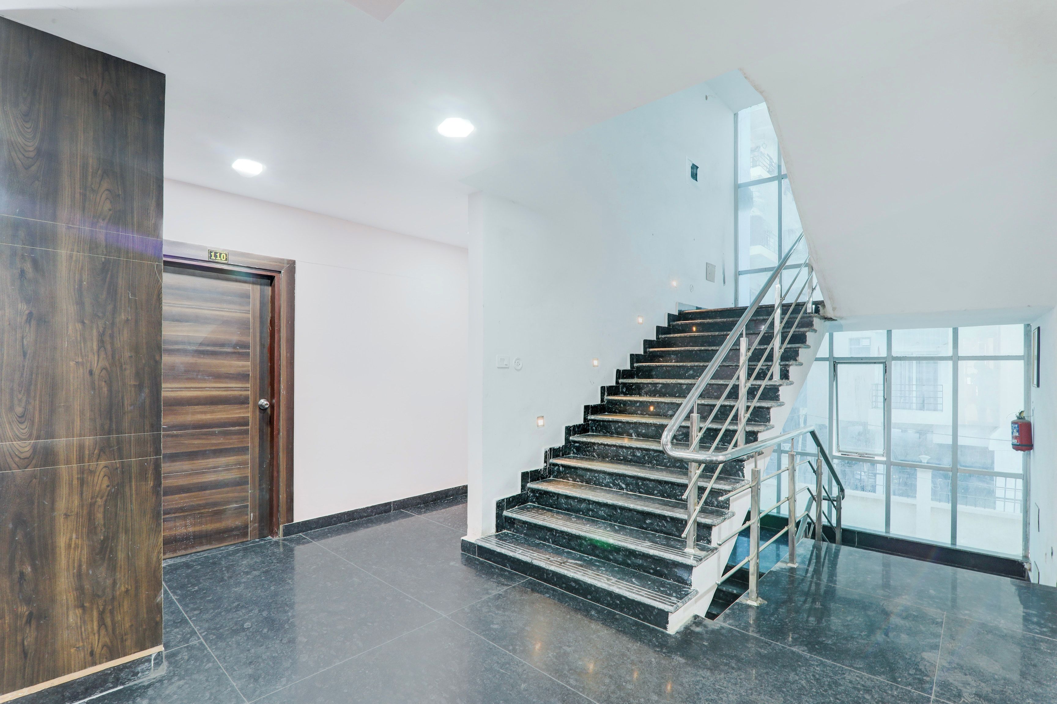 Un interior moderno con una escalera de mármol, una puerta de madera y una pared de vidrio.