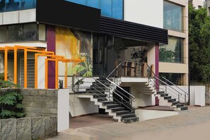 A modern building with a staircase leading to a balcony, surrounded by a stone wall and greenery. - Townhouse Oak HBR Layout (Bengaluru)