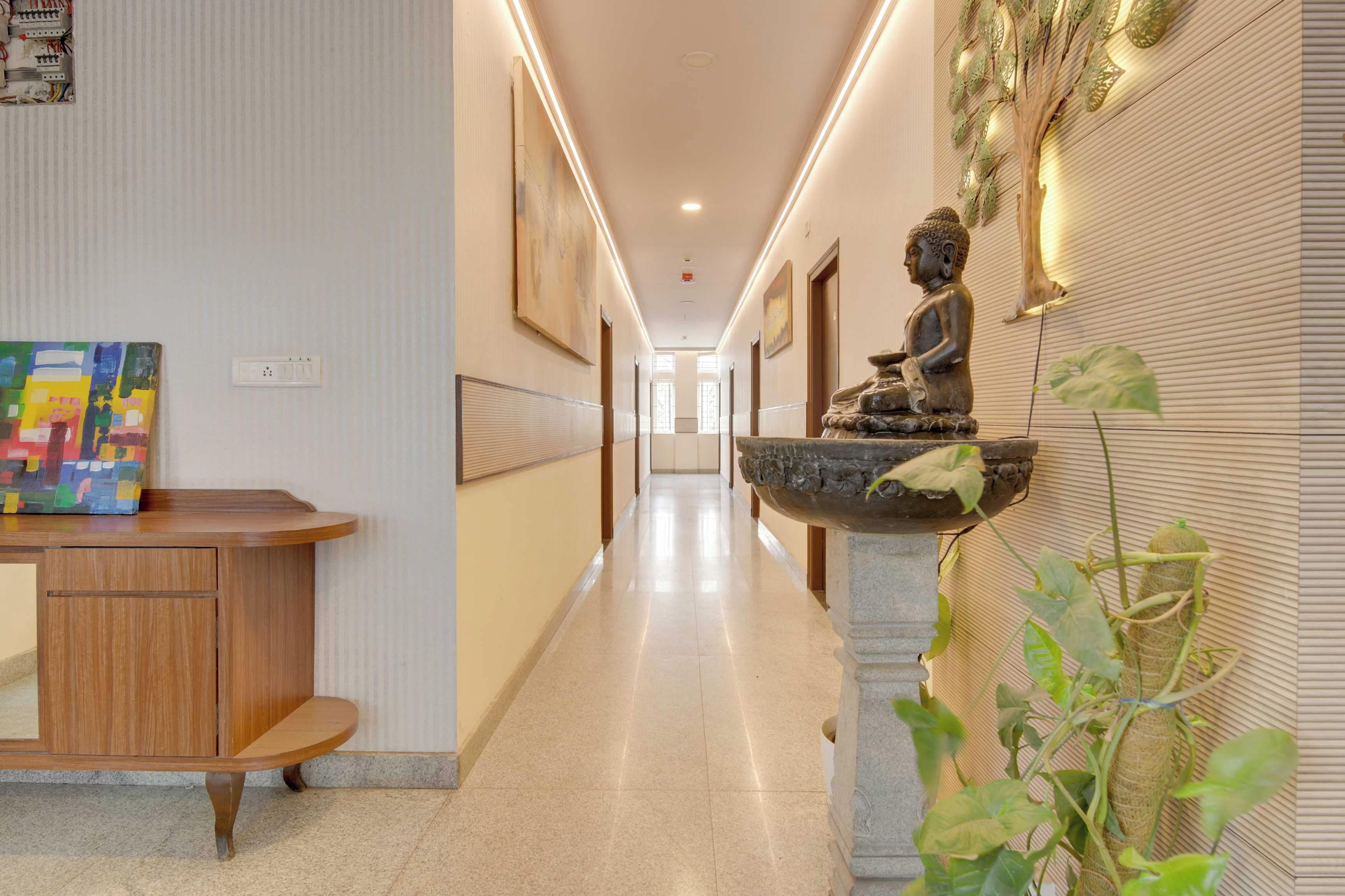 A hotel corridor with a wooden reception desk, a Buddha statue, and a colorful abstract painting.