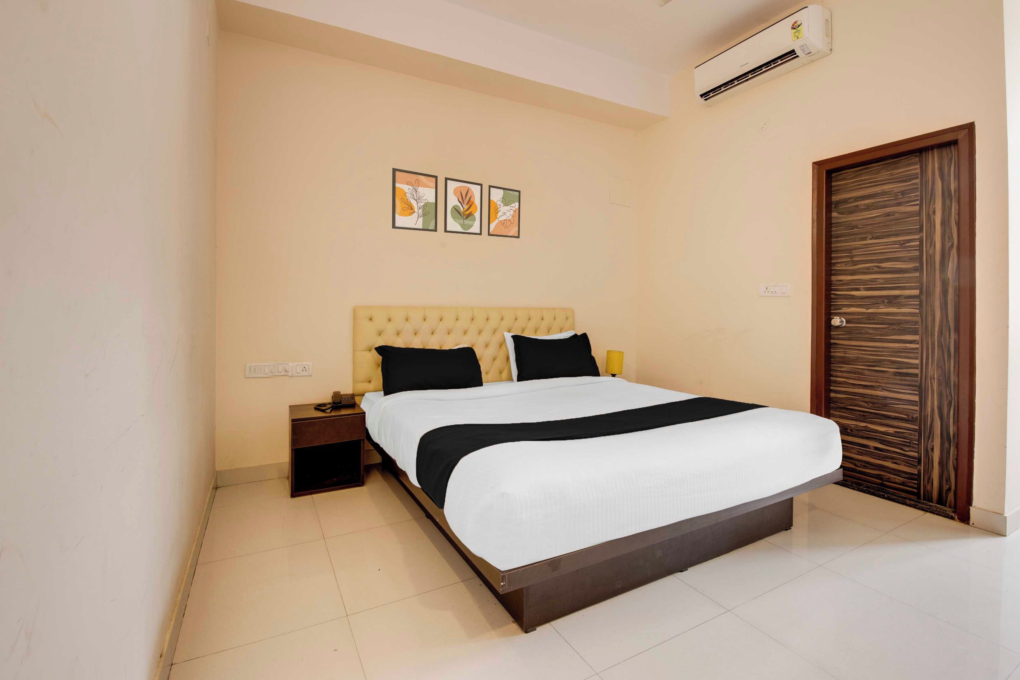 A hotel room with a bed, bedside table, wall art, and a wooden door.