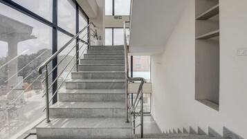 A staircase with metal railings leading to an upper floor, large windows on the left, and a fire exit sign above.