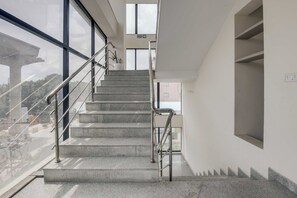 A staircase with metal railings leading to an upper floor, large windows on the left, and a fire exit sign above. - Townhouse Oak HBR Layout (Bengaluru)