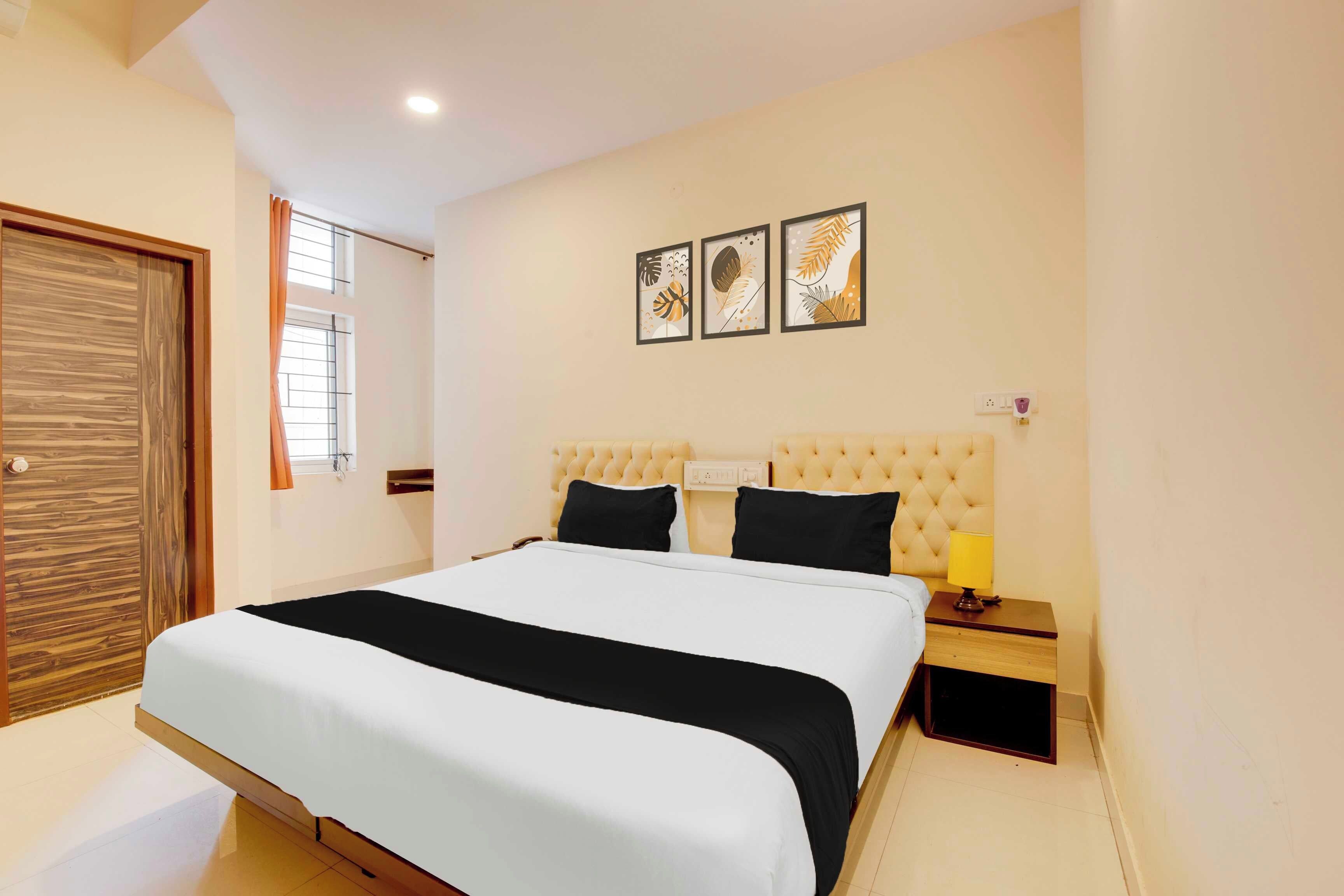 A bedroom with a bed, a nightstand, a lamp, and a wall-mounted power outlet.