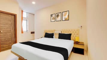 A bedroom with a bed, a nightstand, a lamp, and a wall-mounted power outlet.