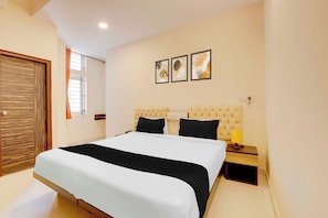 Un dormitorio con cama, mesita de noche, lámpara y toma de corriente en la pared.