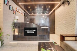A reception area with a black reception desk, clocks on the wall, and a sign indicating the property is company-serviced. - Townhouse Oak HBR Layout (Bengaluru)