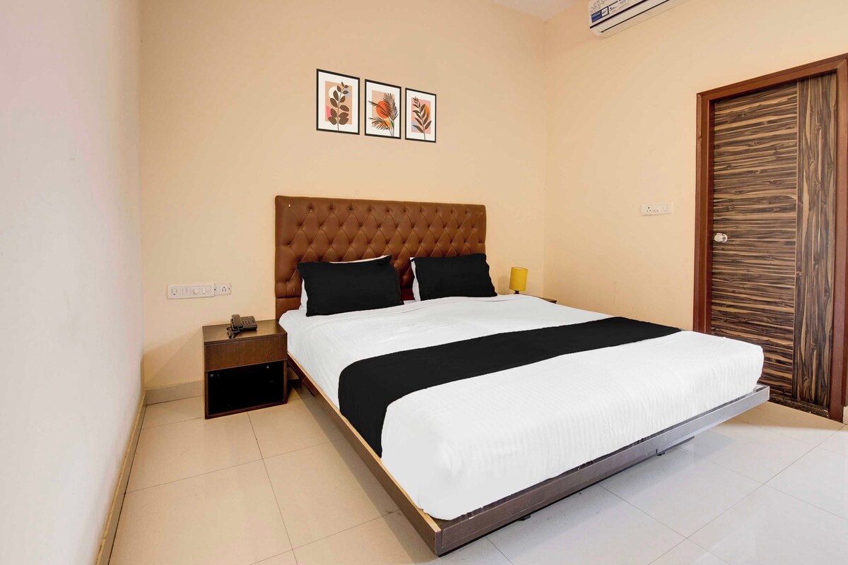 A bedroom with a large bed, a nightstand, a bedside lamp, and a wooden door.